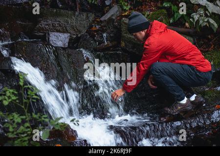 Randonneur sur une longue piste remplit l'eau potable d'une source de montagne dans un récipient en verre. Remplir d'eau propre pour cuisiner et boire tout en étant bien haut Banque D'Images