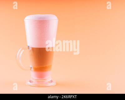 Latte Macchiato dans un verre. Latte macchiato avec mousse rose sur fond de corail. Boisson au café avec lait. Copier l'espace Banque D'Images