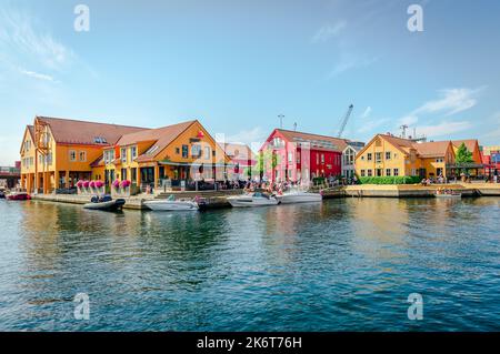 Les gens apprécient une journée ensoleillée à Fiskebrygga (le Fish Wharf) à Kristiansand, Norvège. Bâtiments à façade en bois faisant face au canal et aux bateaux. Banque D'Images