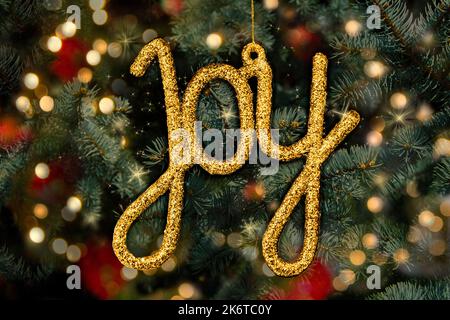 Arbre de Noël avec ornement d'or qui dit Joy, niché dans les branches et les lumières de pin. Carte de vacances. Banque D'Images