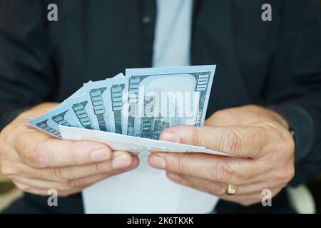 Gros plan de l'homme tenant de l'argent et de l'enveloppe avec des billets de 100 dollars visibles. Banque D'Images