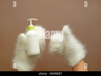 Flacon à pompe cosmétique de lotion hydratante pour tenir les mains dans les mitaines. Banque D'Images
