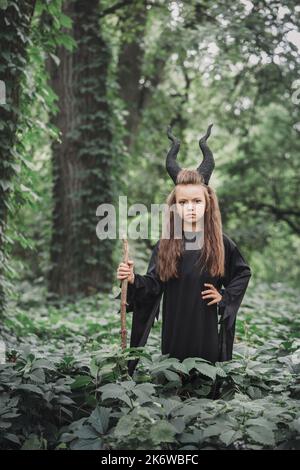 Petite sorcière magique avec de grandes cornes Maleficent dans la forêt. Concept Halloween Banque D'Images