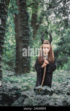 Petite sorcière magique avec de grandes cornes Maleficent dans la forêt. Concept Halloween Banque D'Images