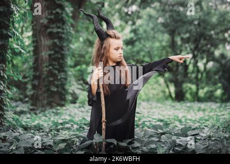 Petite sorcière magique avec de grandes cornes Maleficent dans la forêt. Concept Halloween Banque D'Images