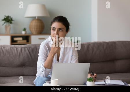 Une femme indienne pensive pense à des idées assis à l'intérieur avec un ordinateur portable Banque D'Images
