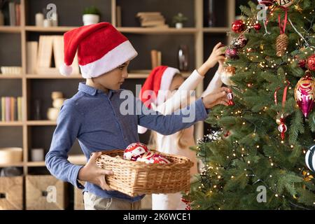 Deux enfants frères dans des chapeaux de père Noël rouges décorant le sapin Banque D'Images