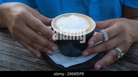 Une femme vêtue d'une robe bleue tient une tasse de café chaud dans ses mains. Ambiance chaleureuse. Gros plan des mains d'une femme d'âge moyen Banque D'Images