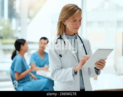 Qui dois-je voir aujourd'hui. une femme médecin mature utilisant une tablette numérique dans un hôpital. Banque D'Images