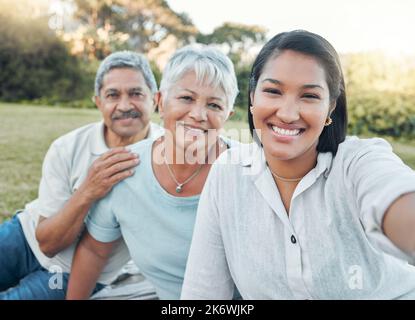 Faire partie d'une famille signifie sourire pour les photos. une femme qui prend un selfie avec ses parents dans un parc. Banque D'Images