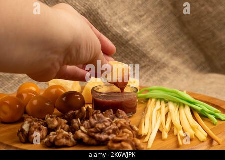 Quelqu'un trempent un morceau de fromage dans le miel sur un fond de variétés variées de fromage Banque D'Images