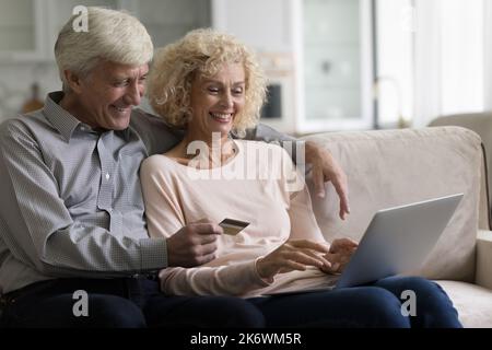 Un couple plus âgé achète sur Internet à l'aide d'un ordinateur portable et d'une carte de débit Banque D'Images