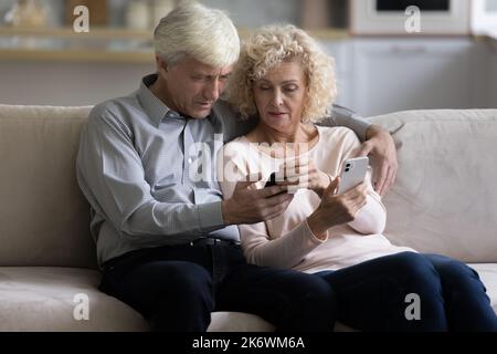 Personnes âgées utilisant deux nouveaux téléphones intelligents modernes achetés à la maison Banque D'Images