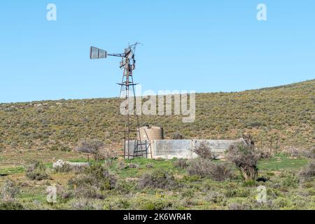 Un moulin à vent cassé, un barrage et un réservoir au-dessus du col d'Ouberg près de Sutherland, dans la province du Cap Nord. Les fleurs de la queue des chats jaunes sont visibles Banque D'Images