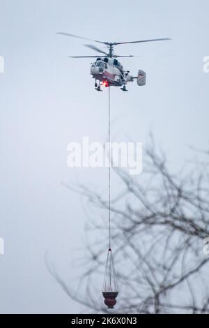 Un hélicoptère d'incendie transporte un conteneur d'eau pour éteindre un incendie dans un bâtiment de production Banque D'Images