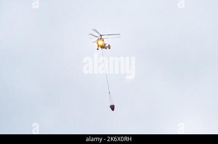 Un hélicoptère d'incendie transporte un conteneur d'eau pour éteindre un incendie dans un bâtiment de production Banque D'Images