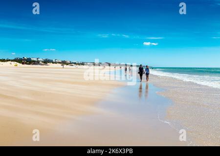 Sable sec balayé par le vent à travers la plage, les gens marchant le long de Playa de la Barrosa, Cadix, Espagne Banque D'Images