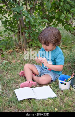 Adorable garçon qui fait ses devoirs sur l'herbe. Un enfant lit un livre dans le parc d'été. Concept de l'apprentissage, de l'étude, de l'extérieur dans le parc. Banque D'Images