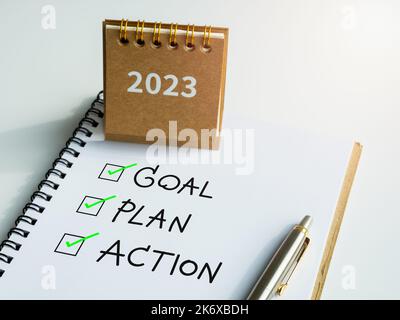 Objectif, plan et action, texte avec coches sur bloc-notes avec stylo et petit calendrier beige de bureau sur fond blanc. Motivation de l'entreprise, résolution, dans Banque D'Images