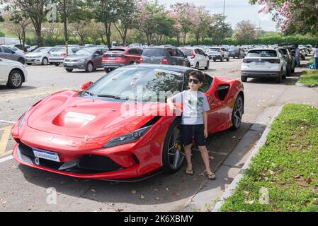 Atibaia - Brésil, 7 octobre 2022: Garçon en lunettes de soleil posant à côté d'une Ferrari F8 Tribto rouge garée. Voiture sport à propulsion intermédiaire. Ferrari - Ital Banque D'Images