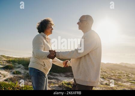 Couple senior souriant tout en dansant ensemble à la plage. Couple de personnes âgées heureux ayant un bon moment à côté de l'océan. Couple romantique appréciant leur r Banque D'Images