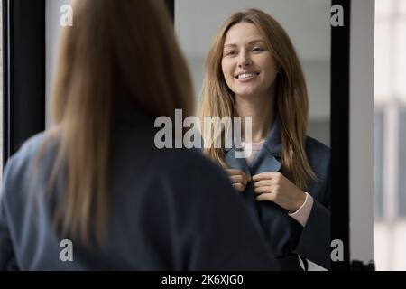 Femme porte un manteau décontracté sombre debout à l'intérieur regarde dans le miroir Banque D'Images