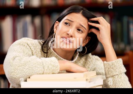 J'ai commencé plus tôt. une jeune étudiante qui a l'air malheureuse en étudiant dans une bibliothèque à l'université. Banque D'Images