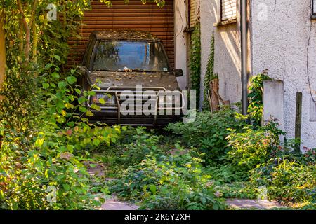 Un vieux SUV est abandonné dans un parking délabré par une maison en besoin de rénovation Banque D'Images