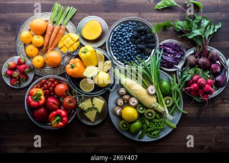 Divers fruits et légumes frais biologiques sur des assiettes métalliques aux couleurs arc-en-ciel sur fond de bois foncé. Banque D'Images