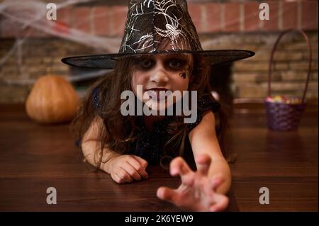 Petite sorcière dans le chapeau de magicien, étire sa main, regarde la caméra avec regard effrayant, jette des sorts. Halloween Banque D'Images