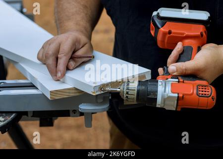 A l'aide d'un tournevis, il fore des trous dans les planches en bois afin des relier les uns aux autres afin qu'ils puissent être utilisés à des fins de construction Banque D'Images