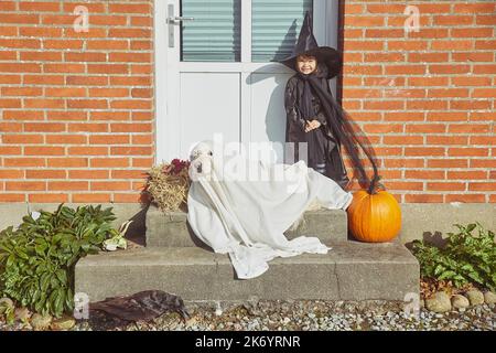 Adorable enfant avec chien sur le porche vêtu de costumes d'halloween Banque D'Images