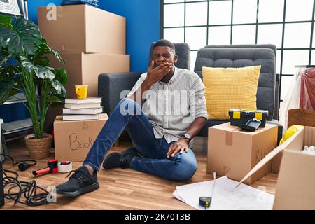L'homme afro-américain assis sur le sol dans une nouvelle maison s'ennuyait bâilling fatigué couvrant la bouche avec la main. agité et somnolence. Banque D'Images