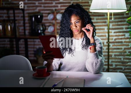 Femme hispanique d'âge moyen utilisant le pavé tactile assis sur la table de nuit bouche et les lèvres fermées comme zip avec les doigts. secret et silencieux, tabou parlant Banque D'Images