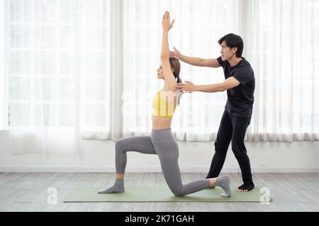 Jeune entraîneur homme d'entraînement femme pratiquant le yoga tout en étirant les mains et l'équilibre dans la salle à la maison, aide instructeur entraînement femme entraînement entraînement y Banque D'Images
