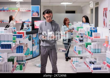 Client indécisif lisant les paquets de médicaments en pharmacie, regardant la bouteille de médicaments et la boîte de médicaments. Vérifier les fournitures pharmaceutiques sur les étagères pour acheter des soins de santé. Banque D'Images