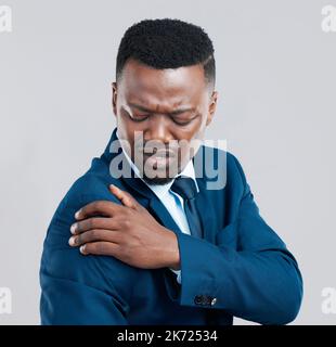 Qu'est-ce que j'ai fait à mon épaule. Photo studio d'un jeune homme d'affaires en situation de tension des épaules sur fond gris. Banque D'Images