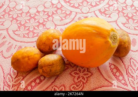 Une papaye et trois prunes de juin sont sur une nappe en dentelle rouge et blanche. Banque D'Images