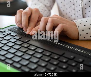 Une femme aveugle utilise un ordinateur avec un écran en braille et un clavier d'ordinateur. Périphérique inclus. Banque D'Images