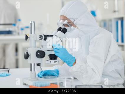 Préparation des échantillons et des échantillons pour des tests ultérieurs. un scientifique portant une combinaison de rayonnement tout en utilisant un microscope dans un laboratoire. Banque D'Images