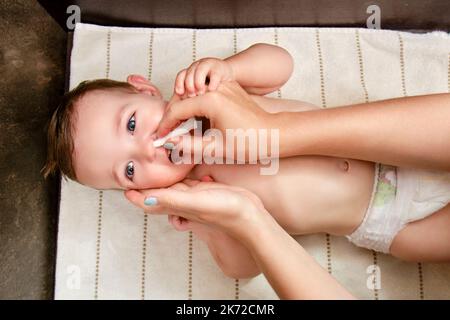 Une mère nettoie son nez avec un tampon en coton torsadé pour un bébé garçon heureux. Maman nettoie les narines d'un enfant souriant. Enfant d'un an Banque D'Images