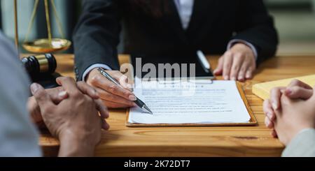 Des hommes d'affaires et des avocats discutent de documents contractuels avec une balance en laiton sur un bureau en bois. Droit, services juridiques, conseils, concept de justice Banque D'Images