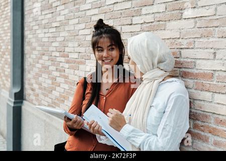 Des amies multiethniques se regardant les unes les autres et souriant tout en étudiant ensemble à l'extérieur. Banque D'Images