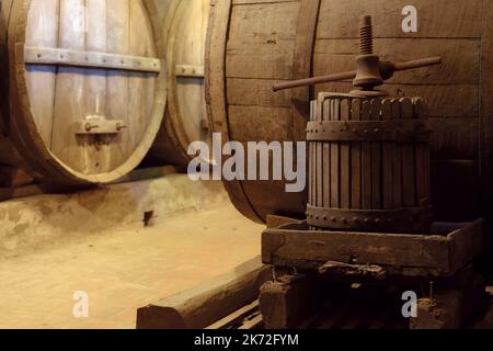 Ancienne cave à vin souterraine avec fûts de chêne en bois pour le vieillissement du vin et presse à vis en premier plan Banque D'Images