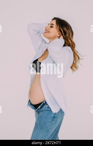 Vue latérale d'une femme qui regarde le ventre de la femme enceinte et qui se pose sur fond blanc Banque D'Images