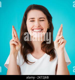 Doigts croisés. Studio photo d'une jeune femme attrayante croisant ses doigts dans l'espoir sur un fond bleu. Banque D'Images