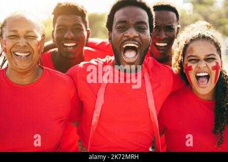 Les fans de sport rouge africains crient tout en soutenant leur équipe - les supporters de football s'amusent lors d'un événement de compétition - concentrez-vous sur le visage de l'homme central Banque D'Images