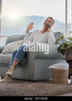 C'est hilarant. Prise de vue en longueur d'une femme sénior qui fait un phonecall tout en se relaxant dans son salon à la maison. Banque D'Images