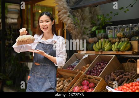 Belle jeune femme épicerie bio magasin portant un tablier tenant des citrouilles dans les mains et souriant à la caméra Banque D'Images