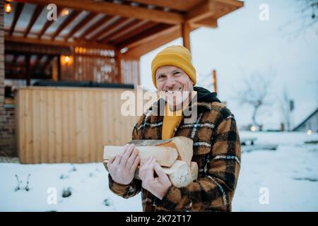 Homme âgé transportant des bûches de bois pour préparer un feu extérieur, pendant la journée d'hiver. Banque D'Images